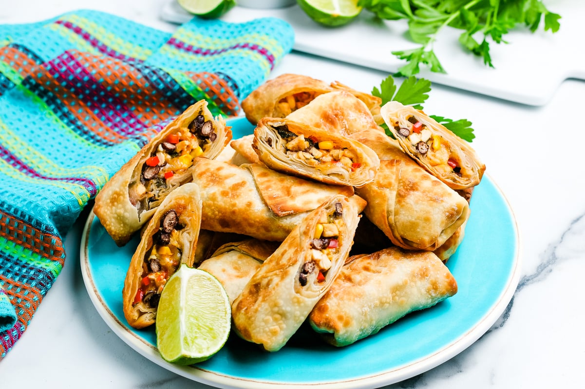 Plate of southwest egg rolls cut open to show the filling of beans, chicken, corn and cheese.
