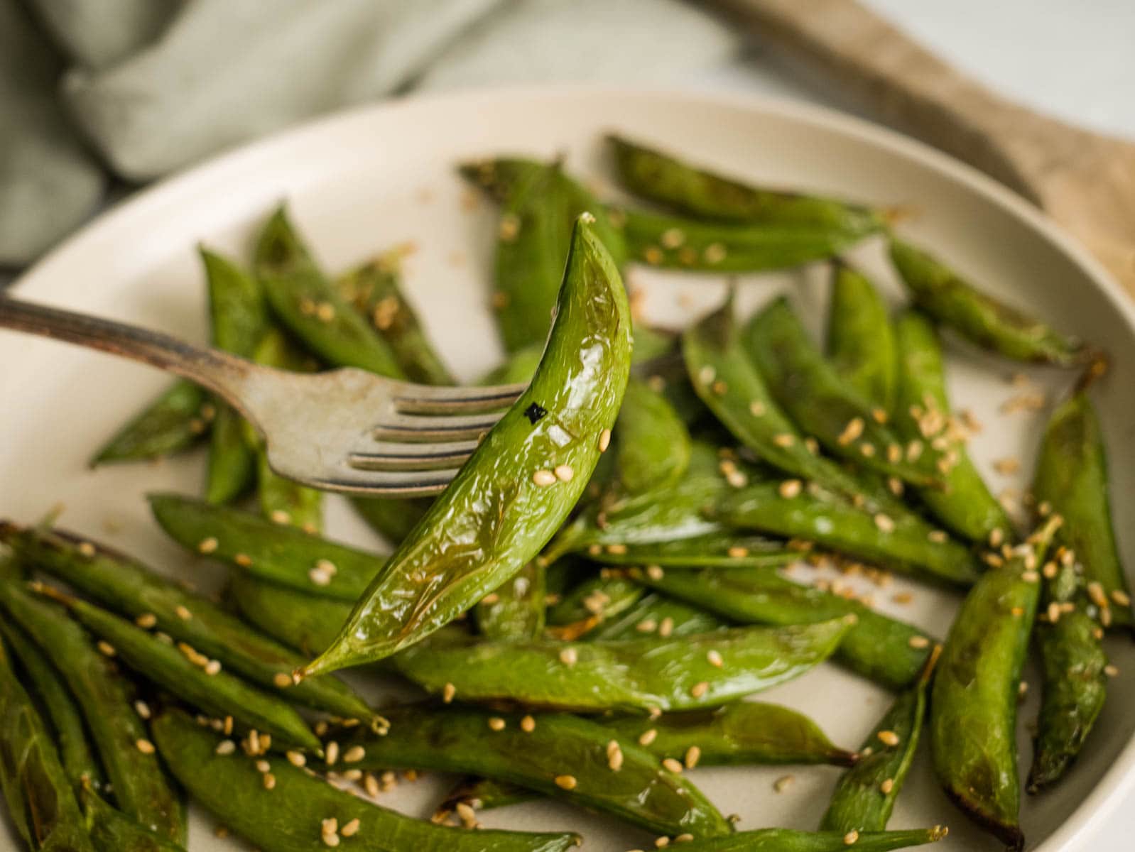 Holding an air fryer snap pea on a fork, after cooking and coating with sesame seeds.