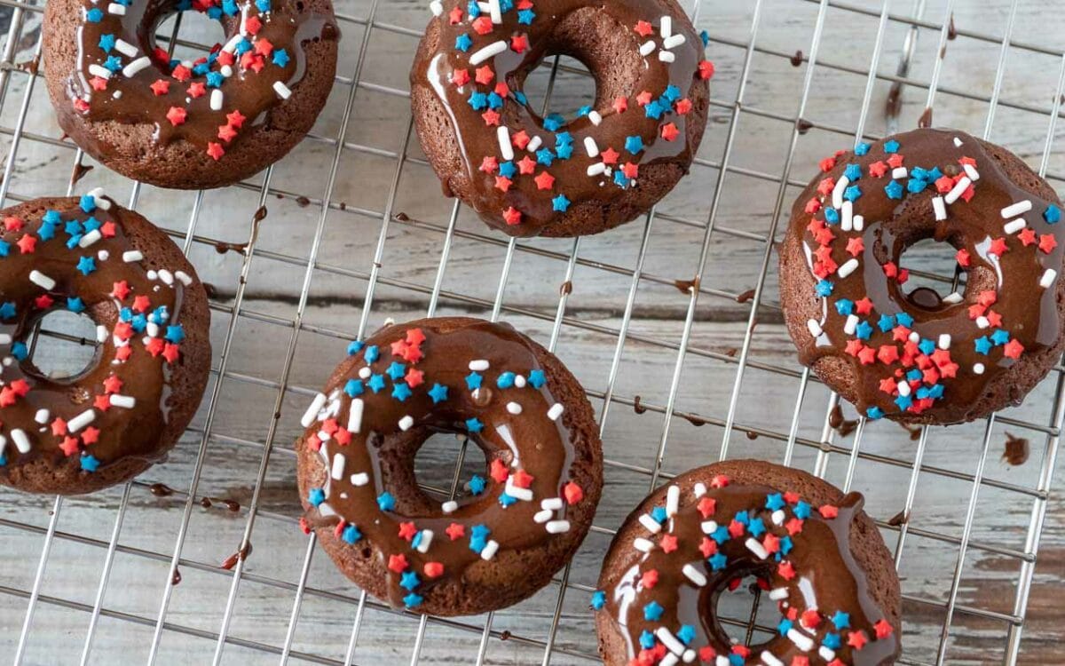 chocolate cake mix donuts with chocolate glaze and red, white and blue sprinkles on a cooling rack.