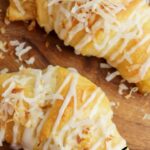 Pineapple crescent rolls topped with glaze and shredded coconut on a wooden surface with text overlays about the recipe.