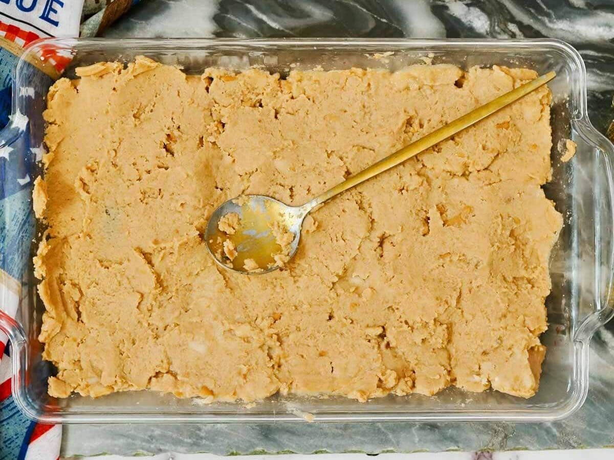 A glass dish containing beans with a gold spoon, partially scooped, on a marble surface.
