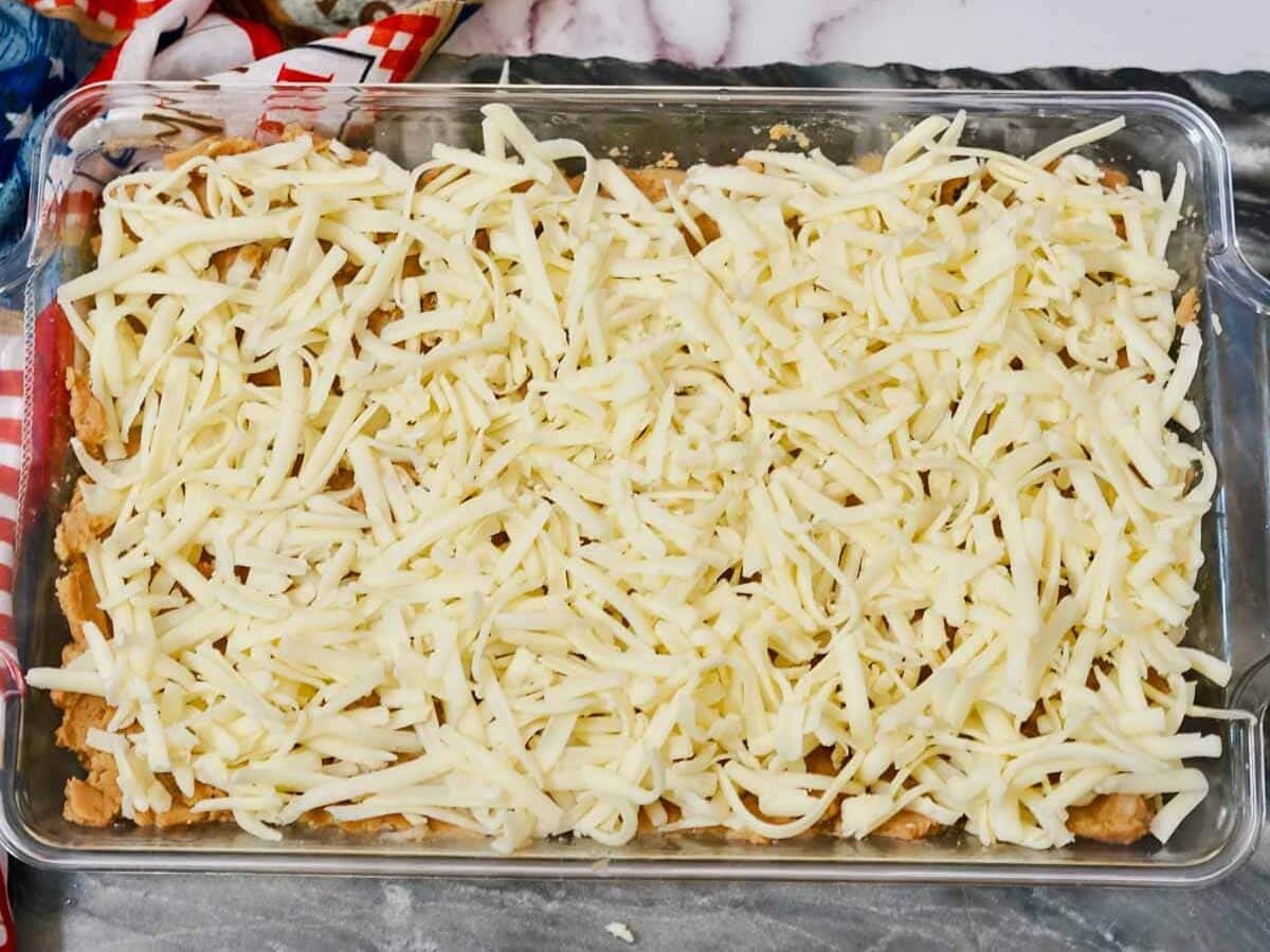 A glass baking dish filled with beans topped with shredded cheese, on a marble countertop.
