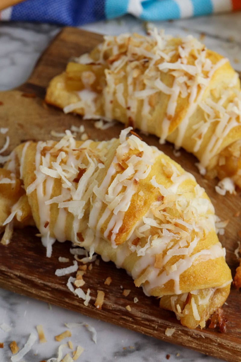 Freshly baked pineapple pastries topped with glaze and shredded coconut on a wooden board.