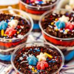 Close-up of festive dessert cups labeled "4th of July Dirt Cups," with layered ingredients, colorful sprinkles, and patriotic-themed decorations. Text on image reads "perfect for kids and adults.