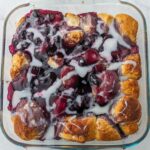 A square glass baking dish filled with a Blueberry Bubble Up topped with glazed dough pieces and drizzled with white icing.