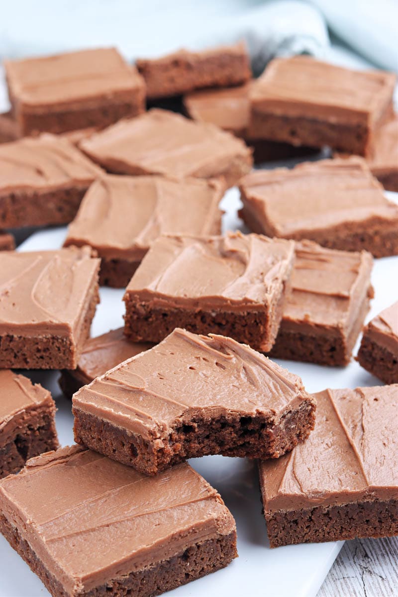 A plate filled with multiple squares of frosted brownies, with a bite taken out of one brownie.