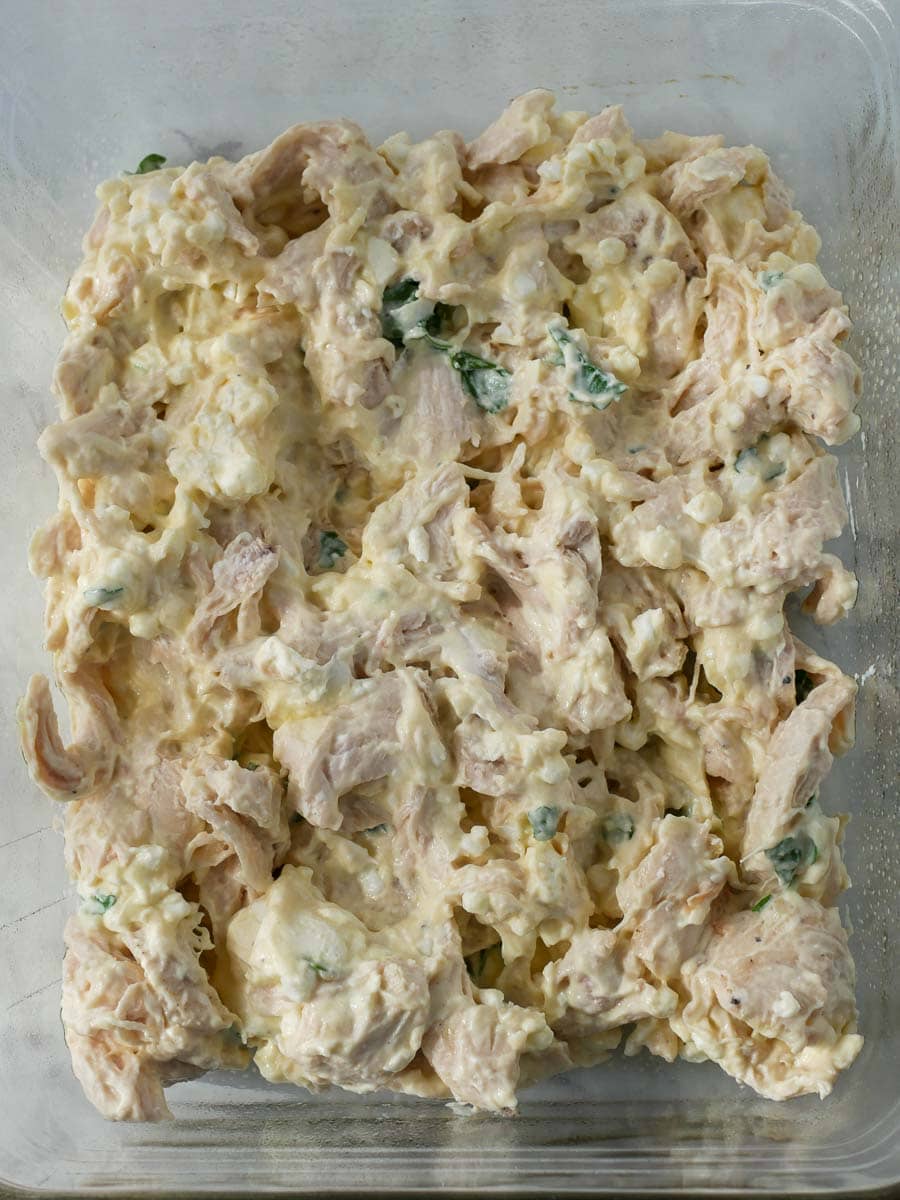 A glass dish containing chicken salad with chunks of chicken, green onions, and a creamy dressing.