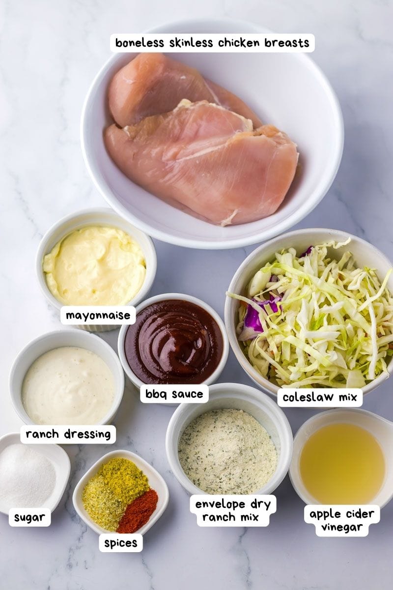 Ingredients on a white countertop: boneless skinless chicken breasts, mayonnaise, coleslaw mix, BBQ sauce, ranch dressing, apple cider vinegar, envelope dry ranch mix, spices, sugar.