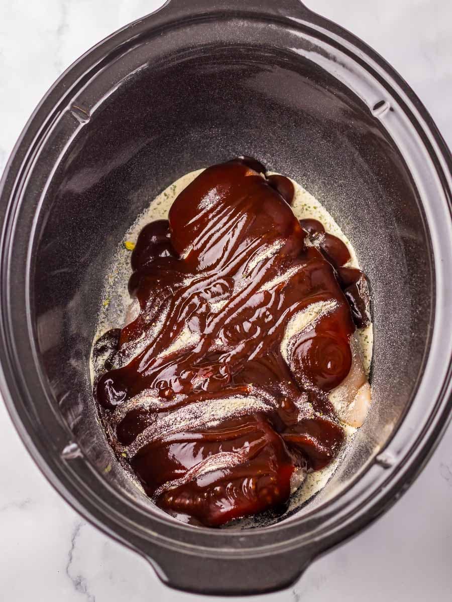 Chicken breasts covered in barbecue sauce inside a slow cooker, ready for cooking.