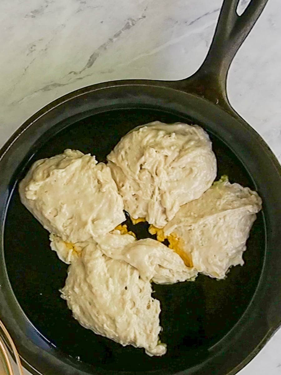 Four portions of raw dough are placed in a cast-iron skillet on a marble countertop.