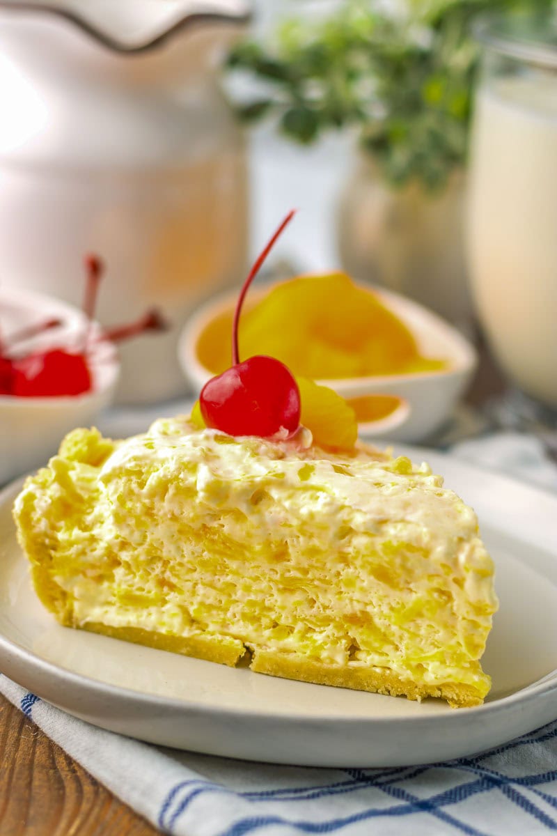 A slice of mandarin orange pie with creamy filling topped with a cherry and served on a white plate.