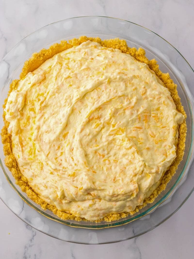 A clear glass pie dish contains an unbaked pie with a vanilla sandwich cookie crust and a creamy mandarin filling.