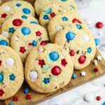 Cookies with red, white, and blue candy and star-shaped sprinkles arranged on a wooden surface, with additional candies scattered around.