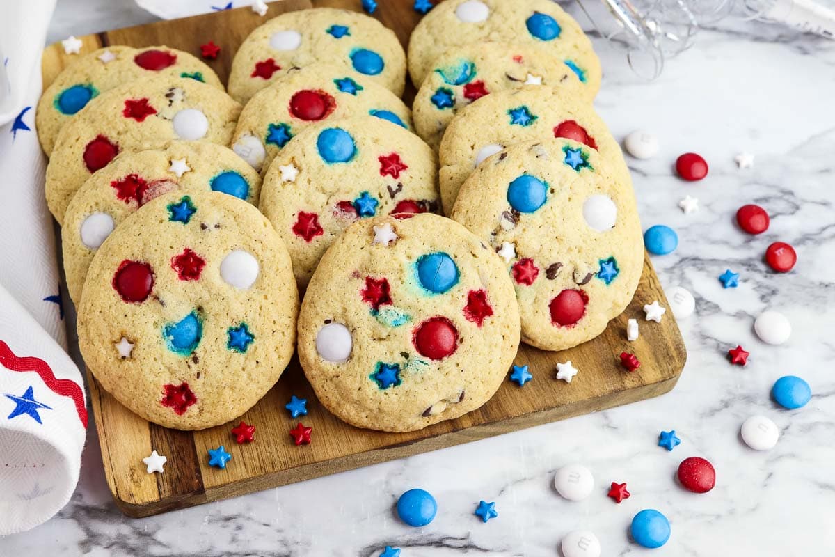Cookies with red, white, and blue candy pieces and star-shaped sprinkles arranged on a wooden board