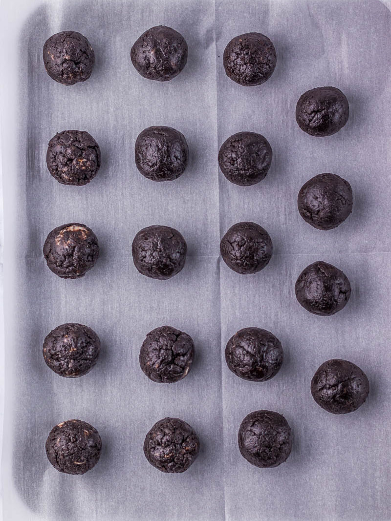 Twenty oreo and cream cheese dough mixture balls arranged in a grid pattern on a baking sheet lined with parchment paper.